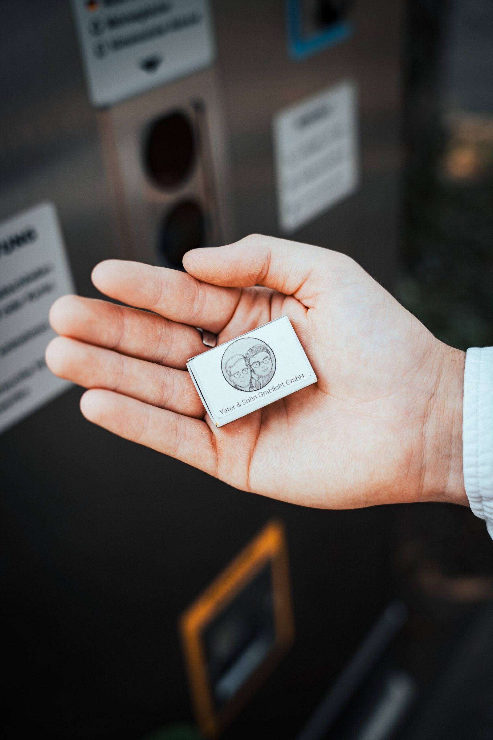 Person hält wasserabweisende Streichholzpackung in der Hand. Vor einem Grablicht Service Point der Firma Vater & Sohn Grablicht GmbH